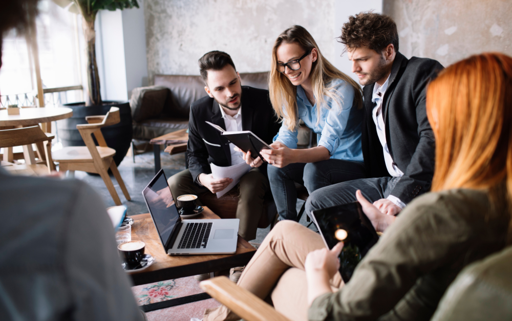 Collega’s bespreken documenten en digitale toestellen tijdens een overleg in een informele kantoorruimte.